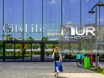 A woman stands in front of an entrance to the CityLife Shopping District in Milan, Italy, on May 27, 2023. (