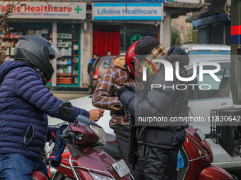 An Indian security personnel checks the identity cards of motorcyclists during a gun battle between militants and security forces on the out...