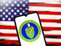 The United States Department of Energy (DOE) logo appears on the screen of a smartphone, and in the background, the flag of the United State...