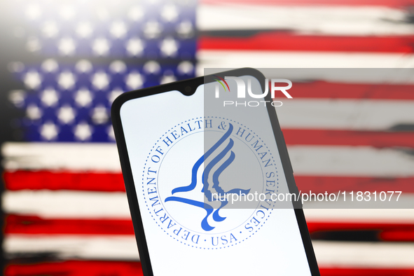 The United States Department of Health and Human Services (HHS) logo appears on the screen of a smartphone, and in the background, the flag...