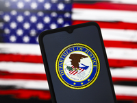 The United States Department of Justice (DOJ) logo appears on the screen of a smartphone, and in the background, the flag of the United Stat...