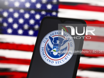 The United States Department of Homeland Security (DHS) logo appears on the screen of a smartphone, and in the background, the flag of the U...