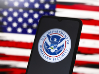 The United States Department of Homeland Security (DHS) logo appears on the screen of a smartphone, and in the background, the flag of the U...