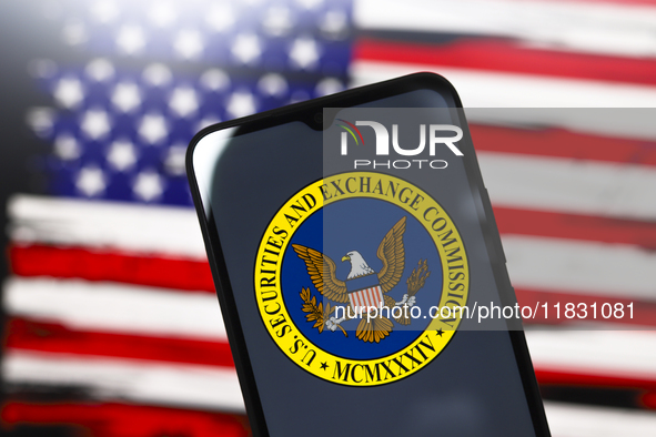 The United States Securities and Exchange Commission (SEC) logo appears on the screen of a smartphone, and in the background, the flag of th...