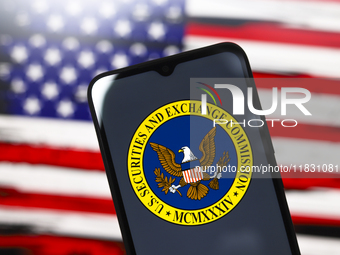 The United States Securities and Exchange Commission (SEC) logo appears on the screen of a smartphone, and in the background, the flag of th...