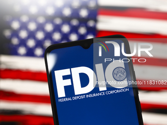 The United States Federal Deposit Insurance Corporation (FDIC) logo appears on the screen of a smartphone, and in the background, the flag o...