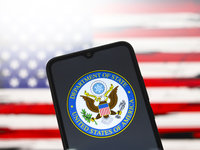 The United States Department of State (DOS) logo appears on the screen of a smartphone, and in the background, the flag of the United States...