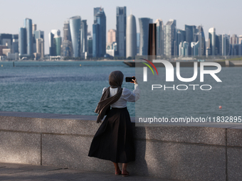 A woman wearing a scarf takes a photo in Doha, Qatar on December 3, 2024. (