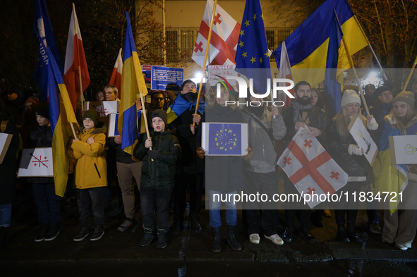 People hold placards as they wave Ukrainian, Georgian, and European Union flags during a rally outside the embassy of Georgia in Warsaw, Pol...