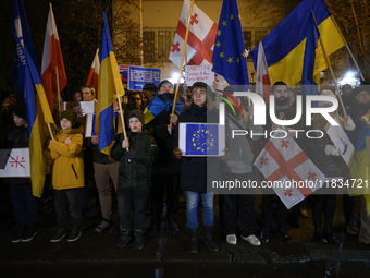 People hold placards as they wave Ukrainian, Georgian, and European Union flags during a rally outside the embassy of Georgia in Warsaw, Pol...