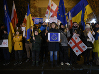 People hold placards as they wave Ukrainian, Georgian, and European Union flags during a rally outside the embassy of Georgia in Warsaw, Pol...