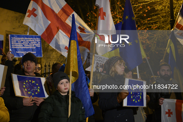 People hold placards as they wave Ukrainian, Georgian, and European Union flags during a rally outside the embassy of Georgia in Warsaw, Pol...