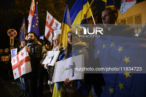 People hold placards as they wave Ukrainian, Georgian, and European Union flags during a rally outside the embassy of Georgia in Warsaw, Pol...