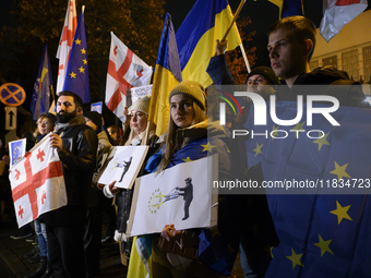 People hold placards as they wave Ukrainian, Georgian, and European Union flags during a rally outside the embassy of Georgia in Warsaw, Pol...