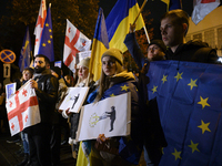 People hold placards as they wave Ukrainian, Georgian, and European Union flags during a rally outside the embassy of Georgia in Warsaw, Pol...