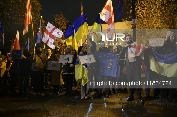 People hold placards as they wave Ukrainian, Georgian, and European Union flags during a rally outside the embassy of Georgia in Warsaw, Pol...