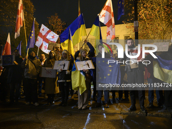 People hold placards as they wave Ukrainian, Georgian, and European Union flags during a rally outside the embassy of Georgia in Warsaw, Pol...