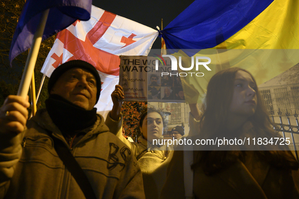 People hold placards as they wave Ukrainian, Georgian, and European Union flags during a rally outside the embassy of Georgia in Warsaw, Pol...