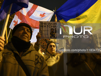 People hold placards as they wave Ukrainian, Georgian, and European Union flags during a rally outside the embassy of Georgia in Warsaw, Pol...