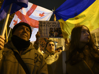 People hold placards as they wave Ukrainian, Georgian, and European Union flags during a rally outside the embassy of Georgia in Warsaw, Pol...