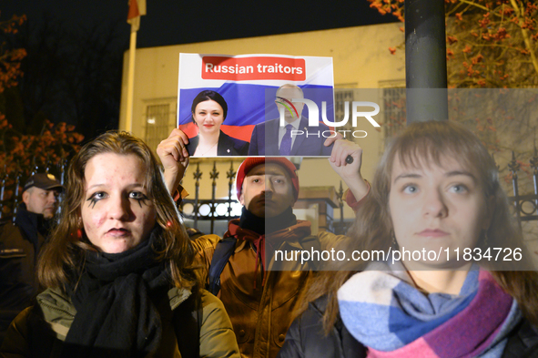 A demonstrator holds a sign depicting members of the Georgian Dream party on a Russian flag as the background during a rally outside the emb...