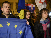 People hold placards as they wave Ukrainian, Georgian, and European Union flags during a rally outside the embassy of Georgia in Warsaw, Pol...