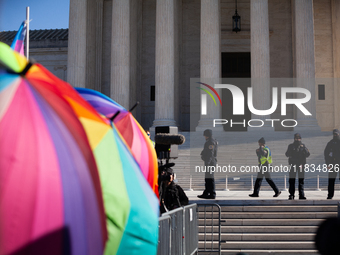 Supreme Court Police patrol the plaza in front of the Court while demonstrators with rainbow umbrellas shield supporters of transgender care...