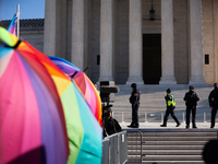 Supreme Court Police patrol the plaza in front of the Court while demonstrators with rainbow umbrellas shield supporters of transgender care...