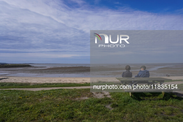 People sit on a bench on the shore of the Wadden Sea, looking at the ebb of the tide in Esbjerg, Jutland, Denmark, on April 28, 2024. 