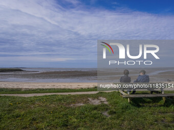 People sit on a bench on the shore of the Wadden Sea, looking at the ebb of the tide in Esbjerg, Jutland, Denmark, on April 28, 2024. (