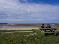 People sit on a bench on the shore of the Wadden Sea, looking at the ebb of the tide in Esbjerg, Jutland, Denmark, on April 28, 2024. (