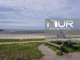 A man sits on a bench on the shore of the Wadden Sea, looking at the ebb of the tide in Esbjerg, Jutland, Denmark, on April 28, 2024. (