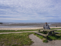 A man sits on a bench on the shore of the Wadden Sea, looking at the ebb of the tide in Esbjerg, Jutland, Denmark, on April 28, 2024. (