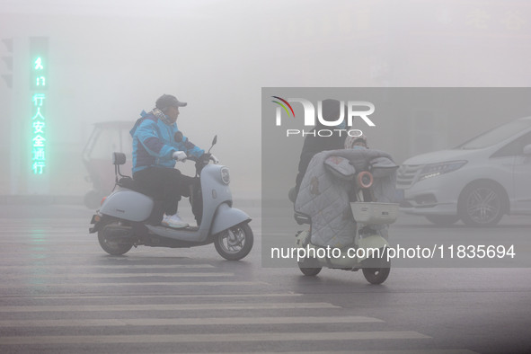 Citizens ride in heavy fog with visibility of less than 100 meters on a street in Hua County, Anyang, China, on December 5, 2024. 