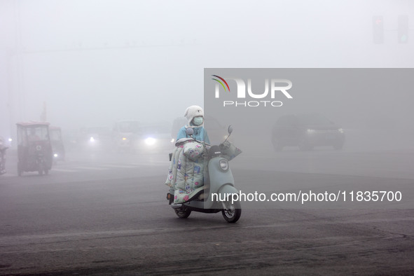 Citizens ride in heavy fog with visibility of less than 100 meters on a street in Hua County, Anyang, China, on December 5, 2024. 