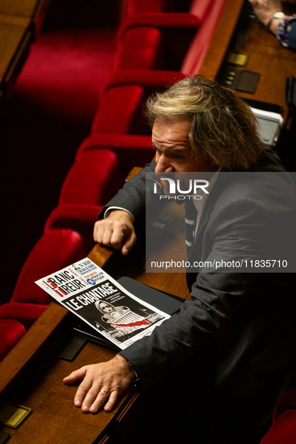 Thierry Sother, deputy of the Socialistes et Apparentes group, holds a newspaper with the headline ''Blackmail'' during the session examinin...