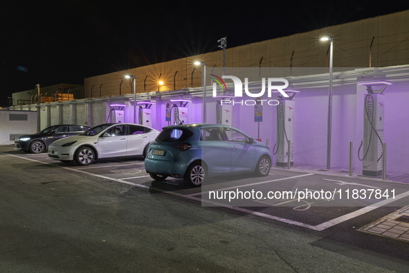 This nighttime image shows an electric vehicle charging station in an urban setting. The charging points are equipped with various models of...