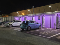 This nighttime image shows an electric vehicle charging station in an urban setting. The charging points are equipped with various models of...