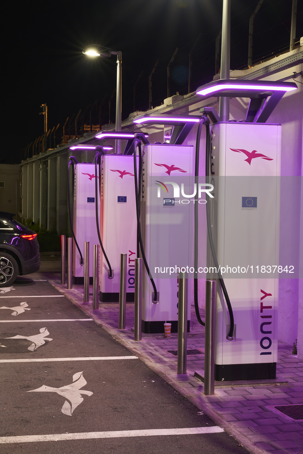 This nighttime image shows an electric vehicle charging station in an urban setting. The charging points are equipped with various models of...