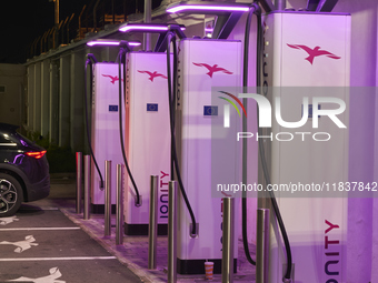 This nighttime image shows an electric vehicle charging station in an urban setting. The charging points are equipped with various models of...