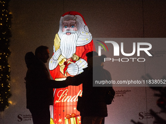 A general view shows tourists standing in front of an illuminated Lindt Santa Claus figure in front of the Lindt Chocolate Museum at the Col...