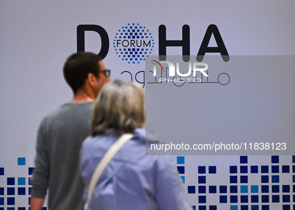 People walk past the Doha Forum logo inside the Sheraton Grand Doha Resort & Convention Hotel ahead of the 22nd edition of the Doha Forum in...