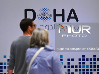 People walk past the Doha Forum logo inside the Sheraton Grand Doha Resort & Convention Hotel ahead of the 22nd edition of the Doha Forum in...