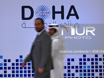 People walk past the Doha Forum logo inside the Sheraton Grand Doha Resort & Convention Hotel ahead of the 22nd edition of the Doha Forum in...