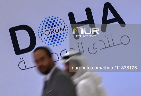 People walk past the Doha Forum logo inside the Sheraton Grand Doha Resort & Convention Hotel ahead of the 22nd edition of the Doha Forum in...