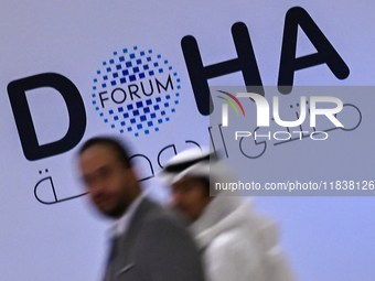 People walk past the Doha Forum logo inside the Sheraton Grand Doha Resort & Convention Hotel ahead of the 22nd edition of the Doha Forum in...