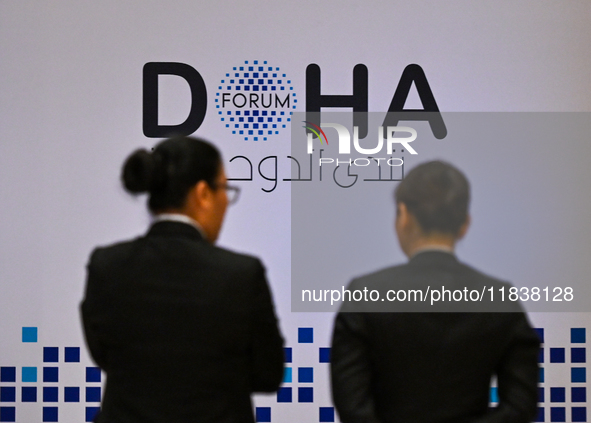 People walk past the Doha Forum logo inside the Sheraton Grand Doha Resort & Convention Hotel ahead of the 22nd edition of the Doha Forum in...