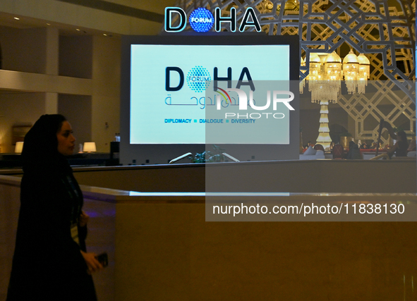 A woman walks past a monitor displaying the Doha Forum logo inside the Sheraton Grand Doha Resort & Convention Hotel ahead of the 22nd editi...