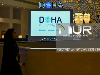 A woman walks past a monitor displaying the Doha Forum logo inside the Sheraton Grand Doha Resort & Convention Hotel ahead of the 22nd editi...