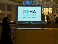 A woman walks past a monitor displaying the Doha Forum logo inside the Sheraton Grand Doha Resort & Convention Hotel ahead of the 22nd editi...